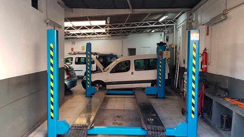 Taller de reparación de automóviles con un vehículo en un elevador; hay otro automóvil y una camioneta presentes.