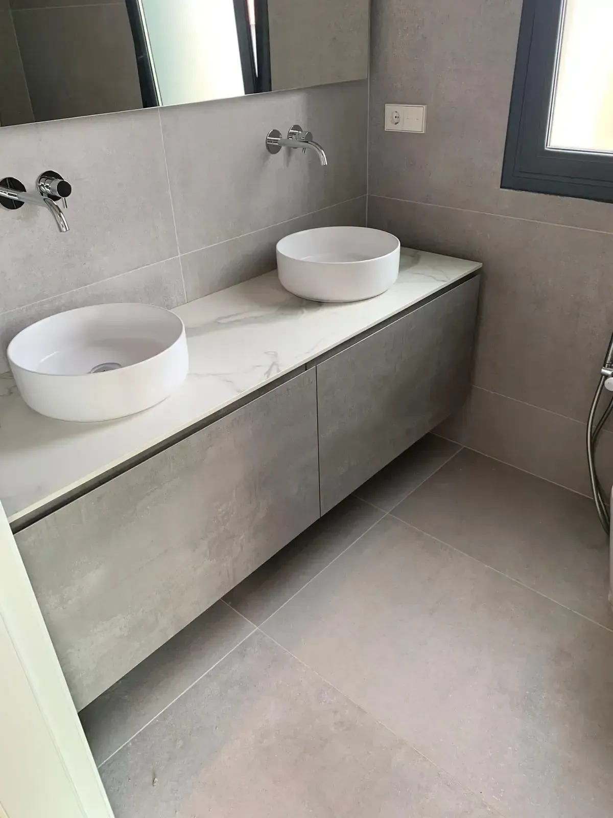 Baño moderno con dos lavabos blancos sobre un mueble gris, paredes grises y suelo a juego.