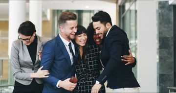 Grupo de cinco empresarios abrazándose en una oficina moderna, celebrando.