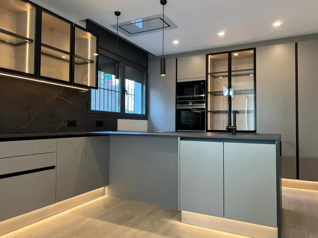 Cocina moderna con gabinetes grises, detalles en negro y vitrinas con frente de vidrio con iluminación.