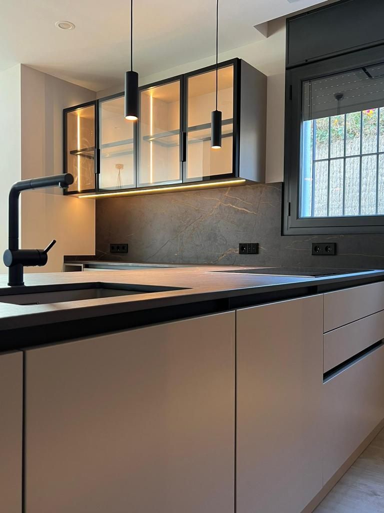 Baño con espejo ovalado retroiluminado, azulejos en espiga gris, lavabo blanco y tocador de madera.