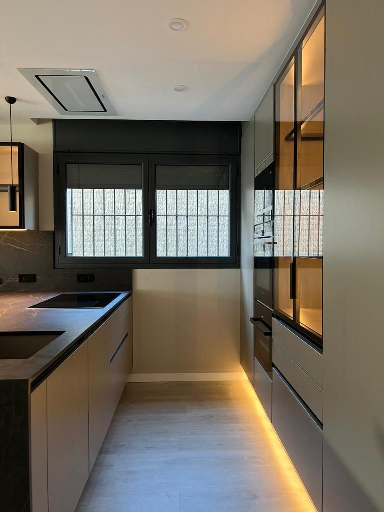 Cocina moderna con gabinetes grises, detalles en negro y vitrinas con frente de vidrio con iluminación.