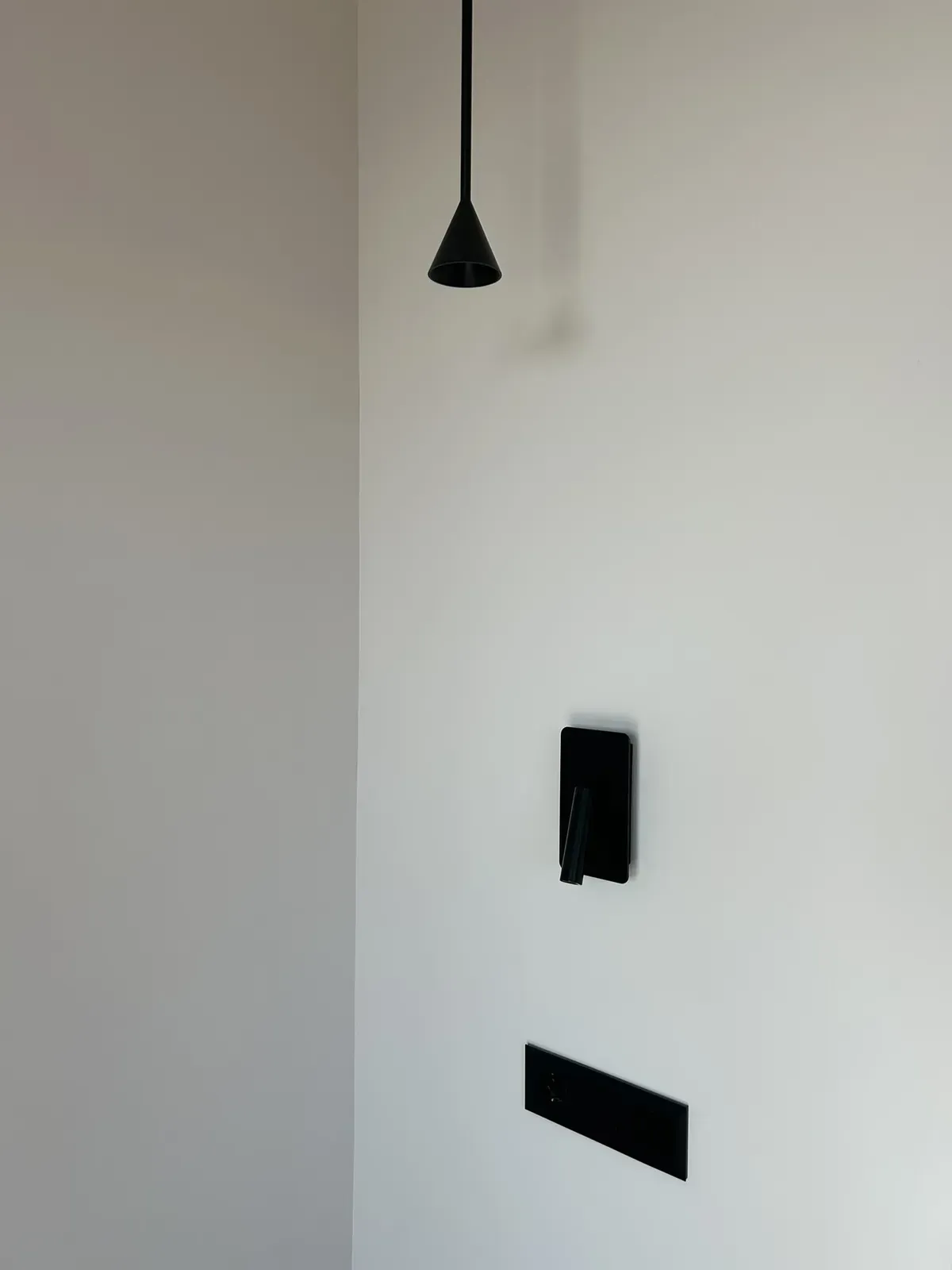 Paredes blancas, lámpara negra, altavoz y ventilación rectangular.