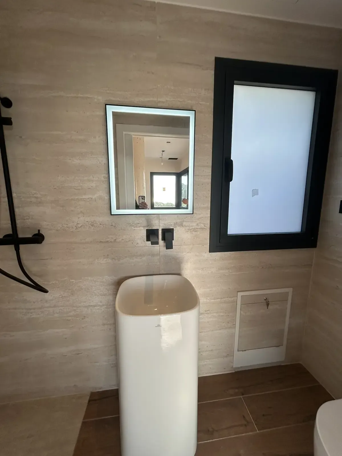 Baño moderno con lavabo de pedestal, espejo cuadrado, marco de ventana negro y paredes beige.