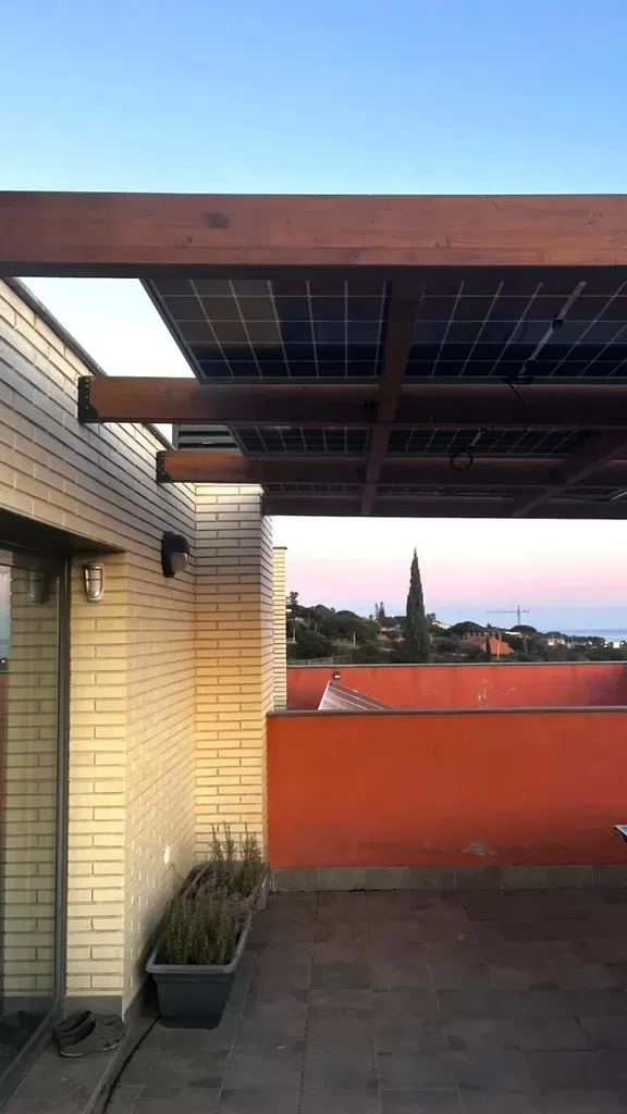 Terraza en la azotea con paneles solares encima, pared de ladrillo, pared naranja y plantas en macetas.