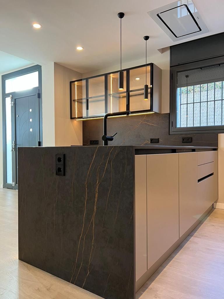 Cocina moderna con gabinetes de colores claros, encimeras oscuras, electrodomésticos empotrados.