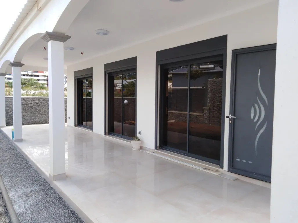 Porche couvert avec sol carrelé blanc et portes vitrées foncées le long d'une façade de maison moderne