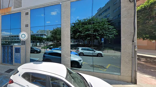 Un coche blanco está aparcado delante de un edificio con muchas ventanas.