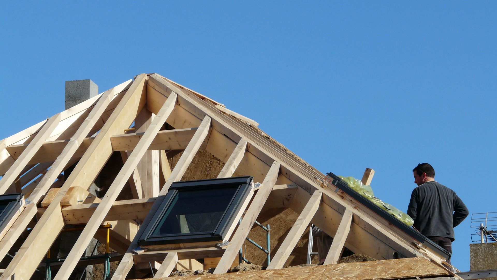 Charpente de toit en construction avec des ouvriers et une lucarne sur fond de ciel bleu