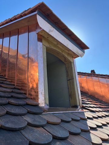 Toiture en tuiles de terre cuite rouge à nervures diagonales et petite ouverture de ventilation.