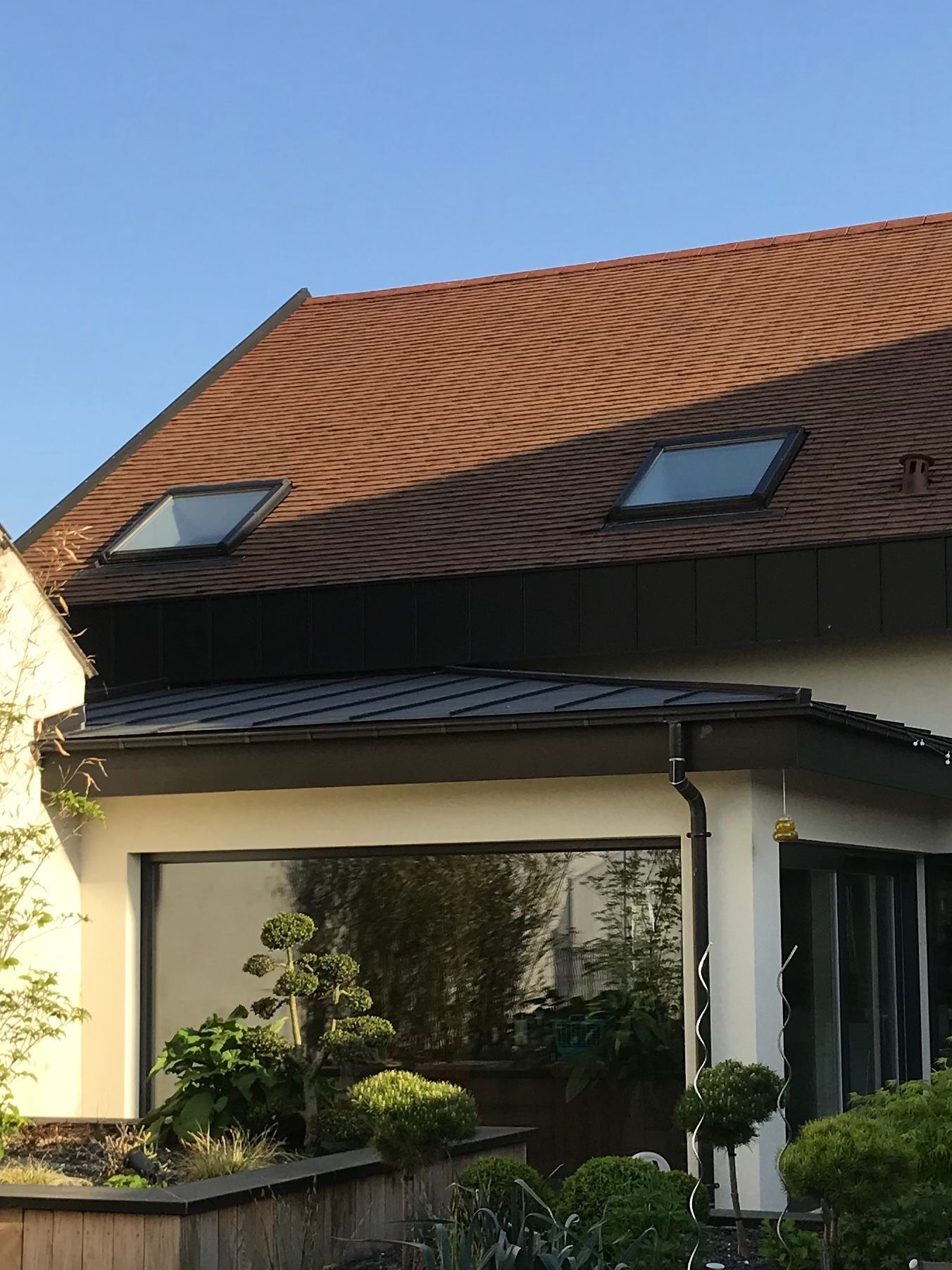 Extérieur d'un bâtiment en briques avec une applique murale éclairée à côté d'un toit en métal gris au crépuscule