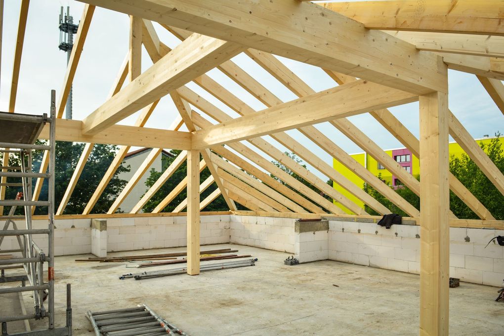 Charpente de toit en bois en construction à l'intérieur d'une maison, avec échafaudages et murs inachevés.