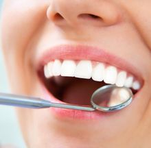 Primer plano de una boca sonriente con un espejo dental examinando dientes blancos.