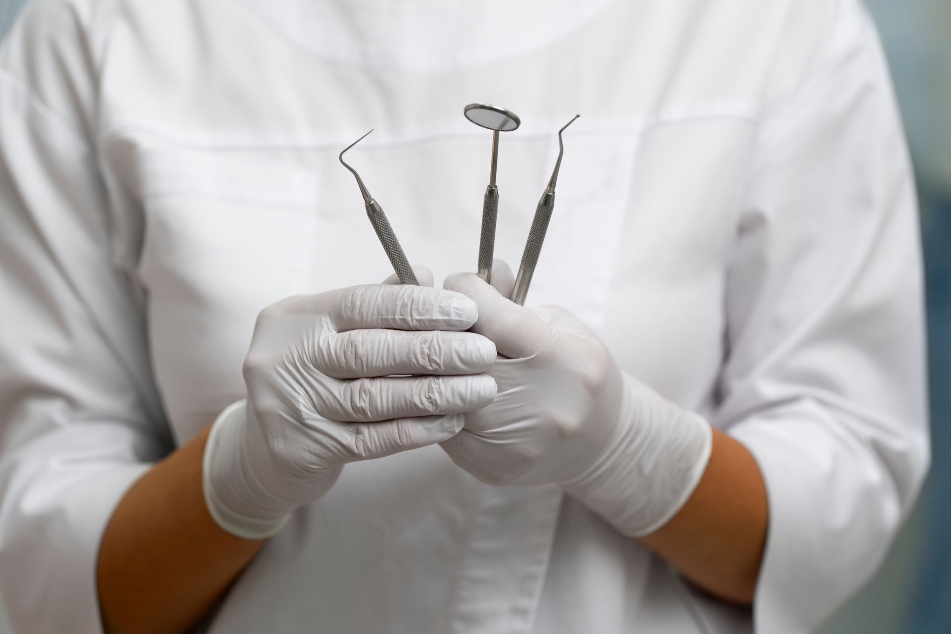 Manos enguantadas sosteniendo instrumentos dentales frente a una bata blanca de laboratorio.