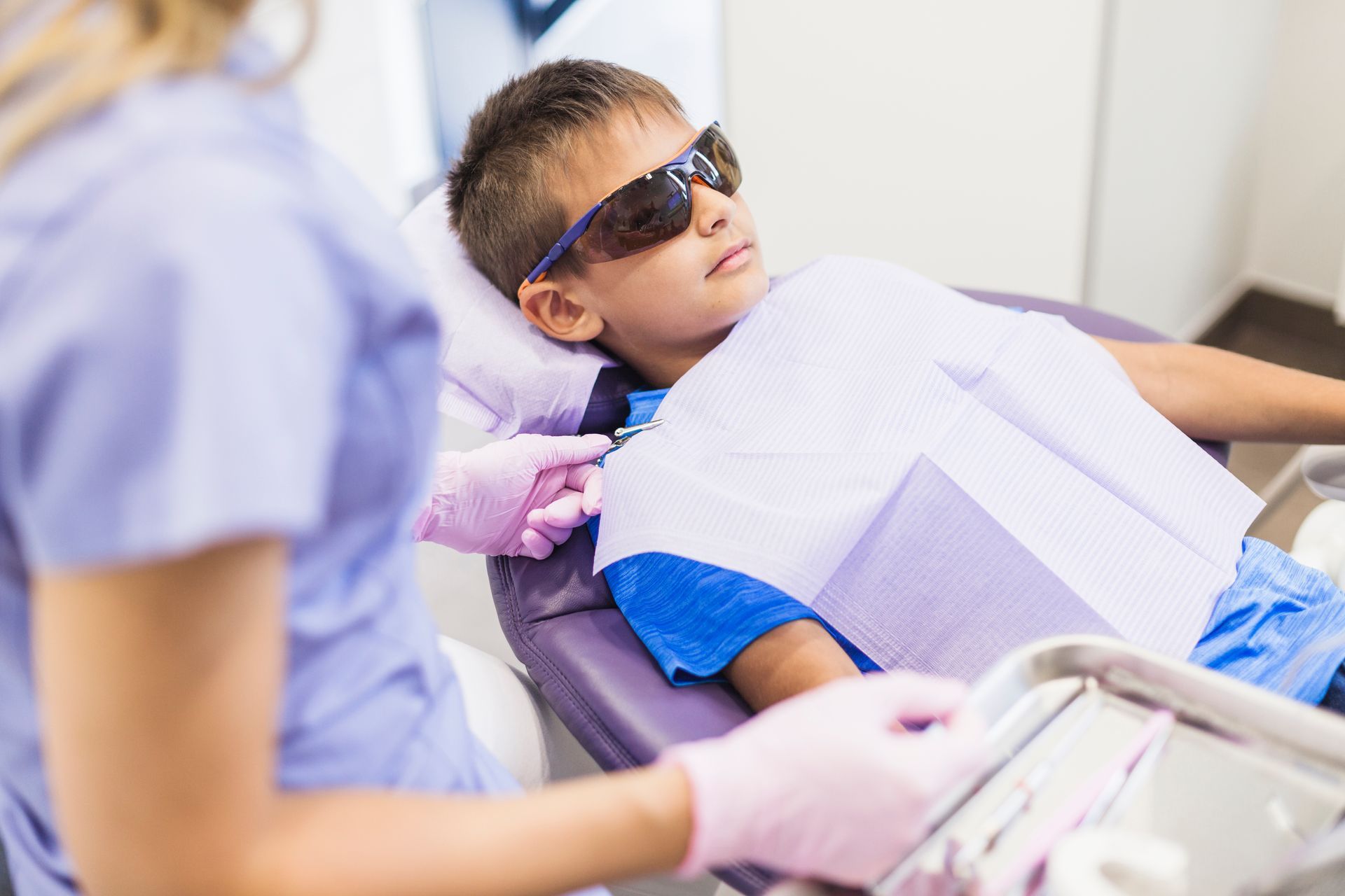 Un niño lleva gafas de sol en una cita con el dentista mientras está reclinado en una silla.