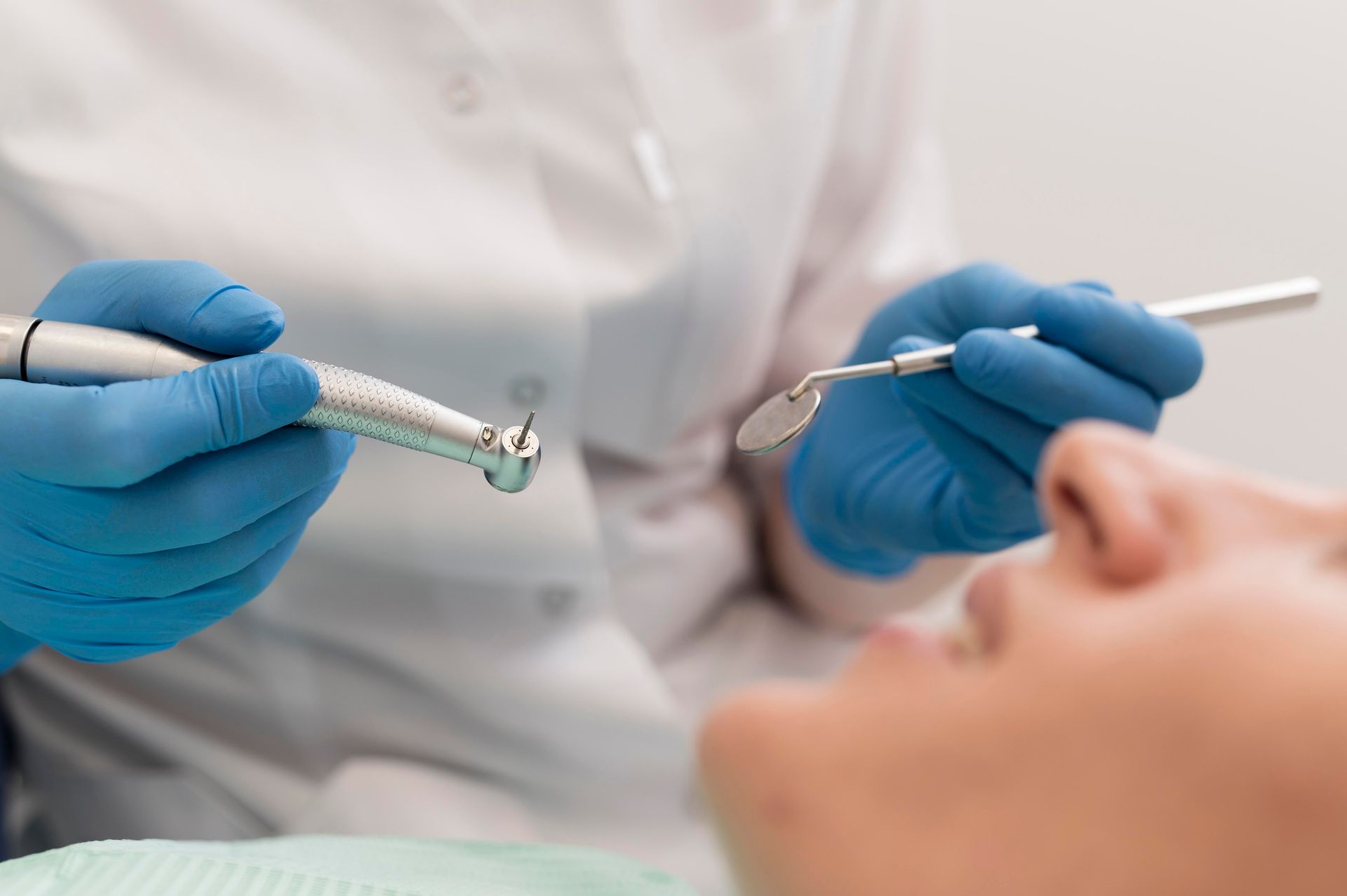 Dentista con guantes azules sosteniendo instrumentos cerca de un paciente recostado en un sillón dental.