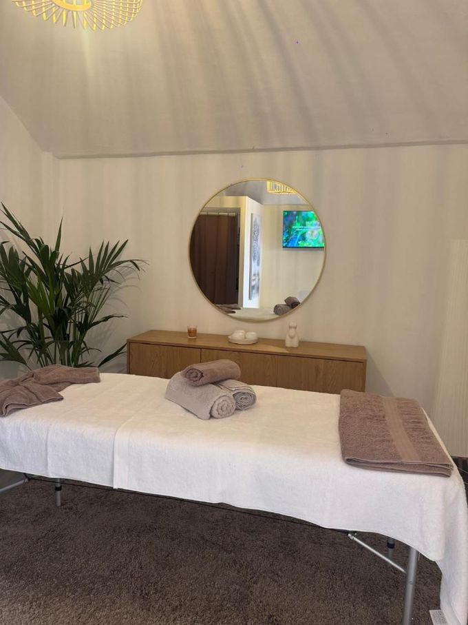 Habitación de hotel con dos camas individuales, cómoda de madera, espejo redondo, planta en maceta y televisor