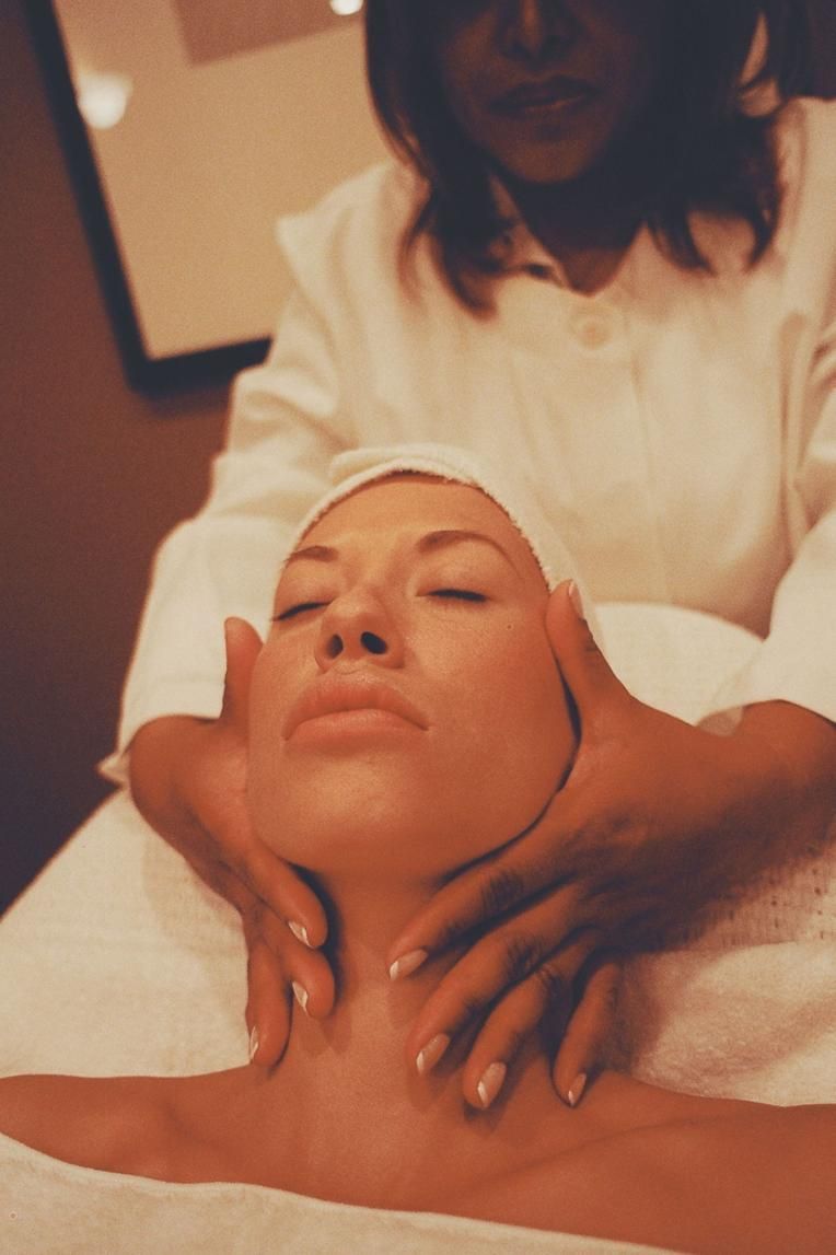Masaje facial con una persona recostada y otra aplicando las manos en el cuello y la mandíbula.