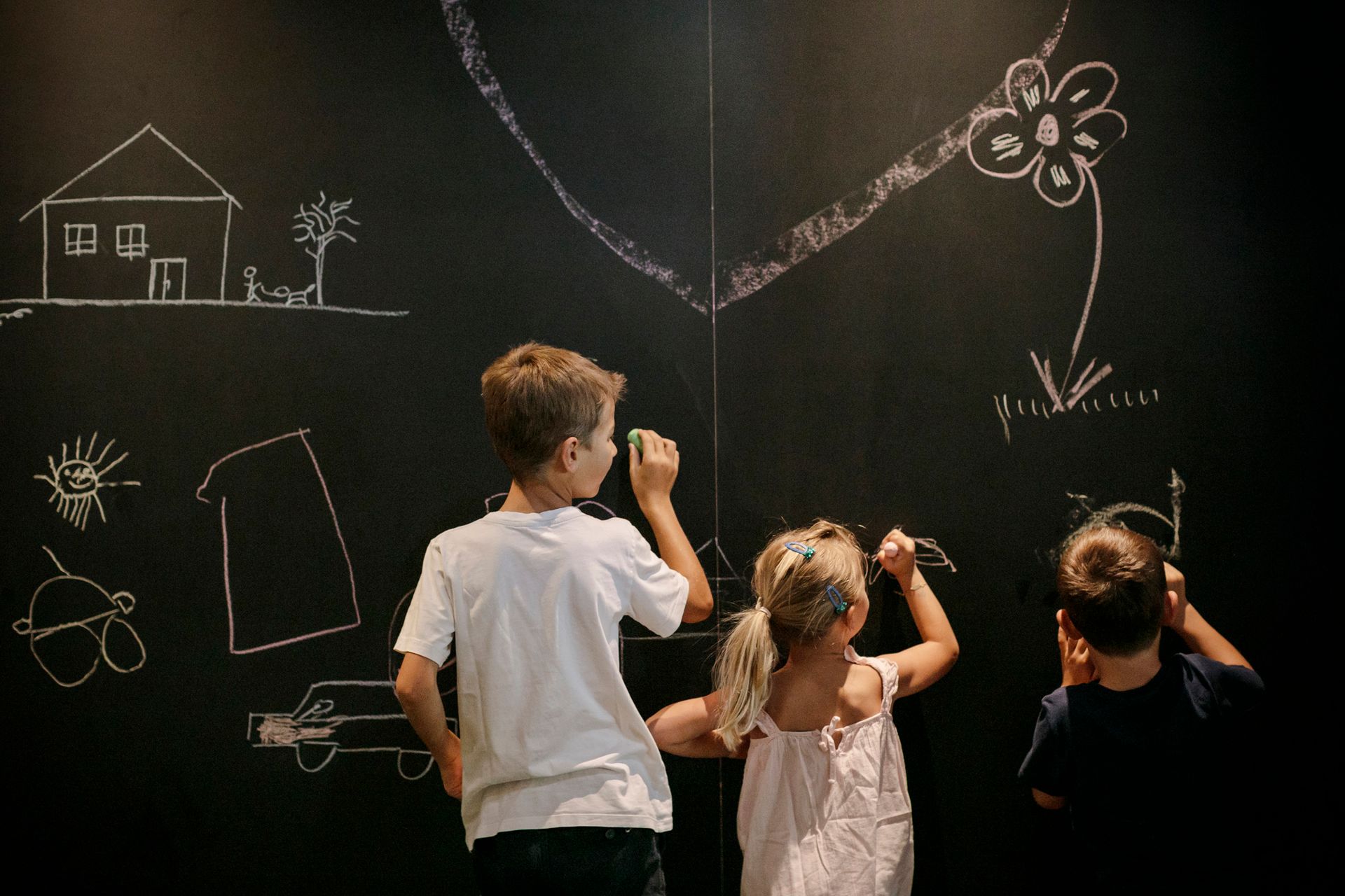 Drei Kinder schreiben mit Kreide an einer Tafel .