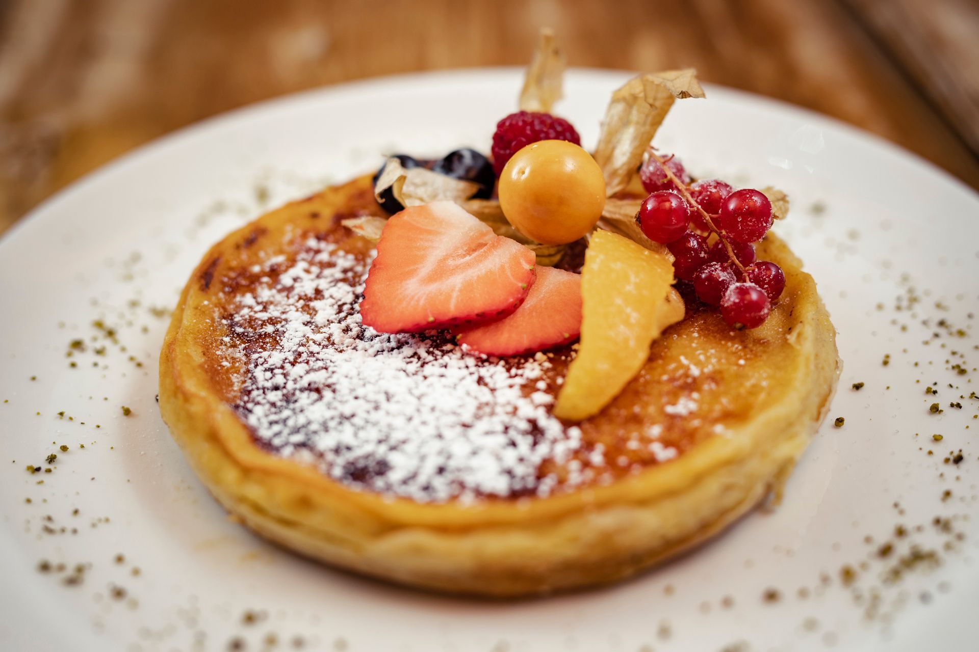 Auf einem weißen Teller steht ein Pfannkuchen mit Obst und Zuckerguss .