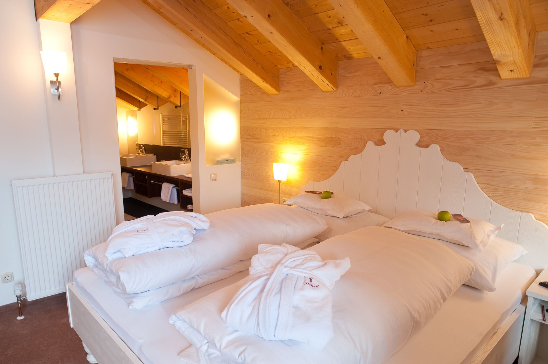Stäfeli Zimmer mit weißem Holzbett und Blick in das Badezimmer