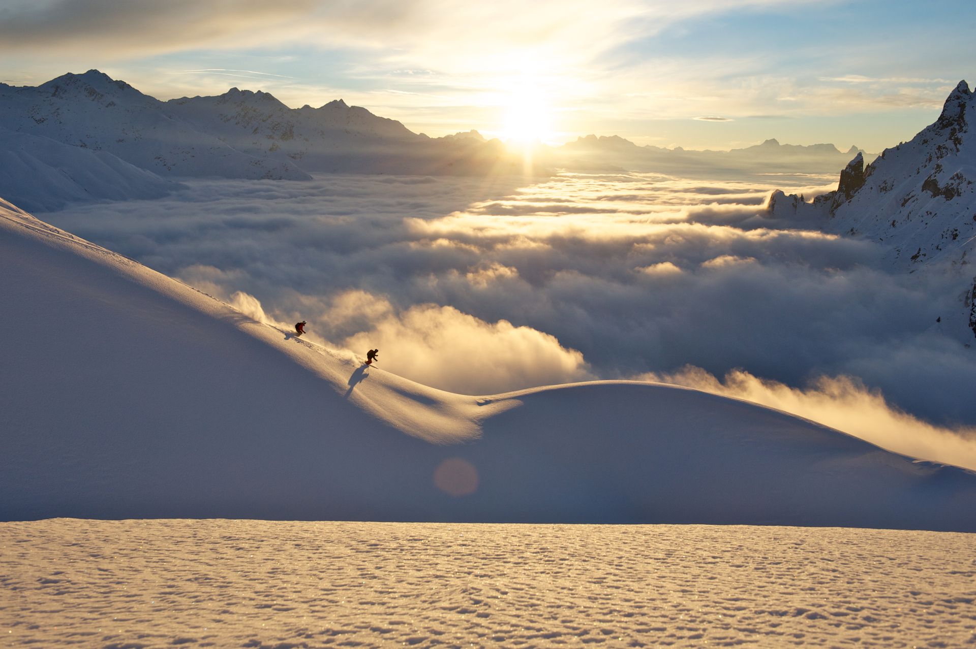 Zwei Skifahrer fahren bei Sonnenuntergang auf einem schneebedeckten Berg .