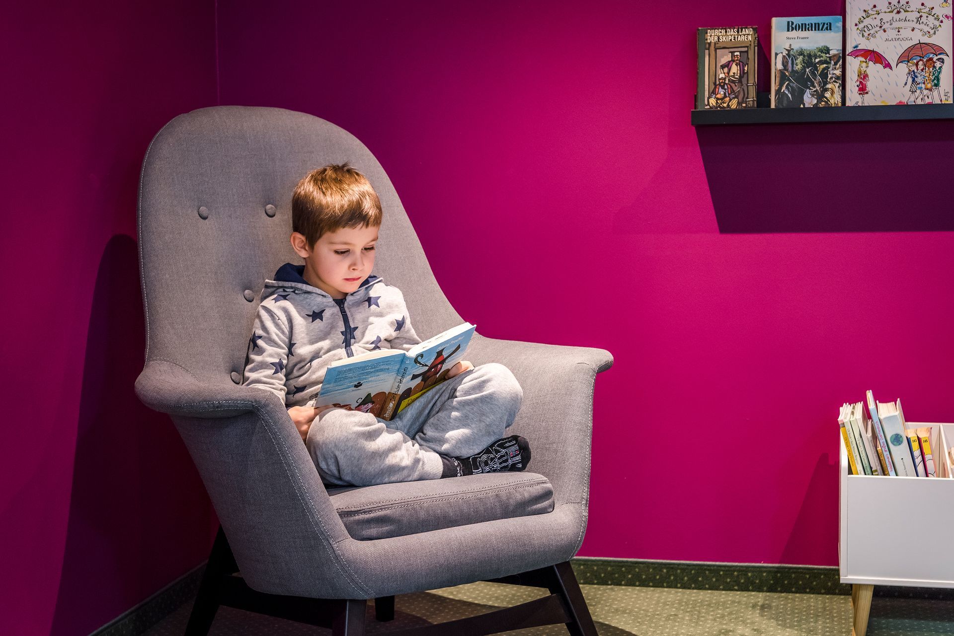Ein kleiner Junge sitzt in einem Stuhl und liest ein Buch .