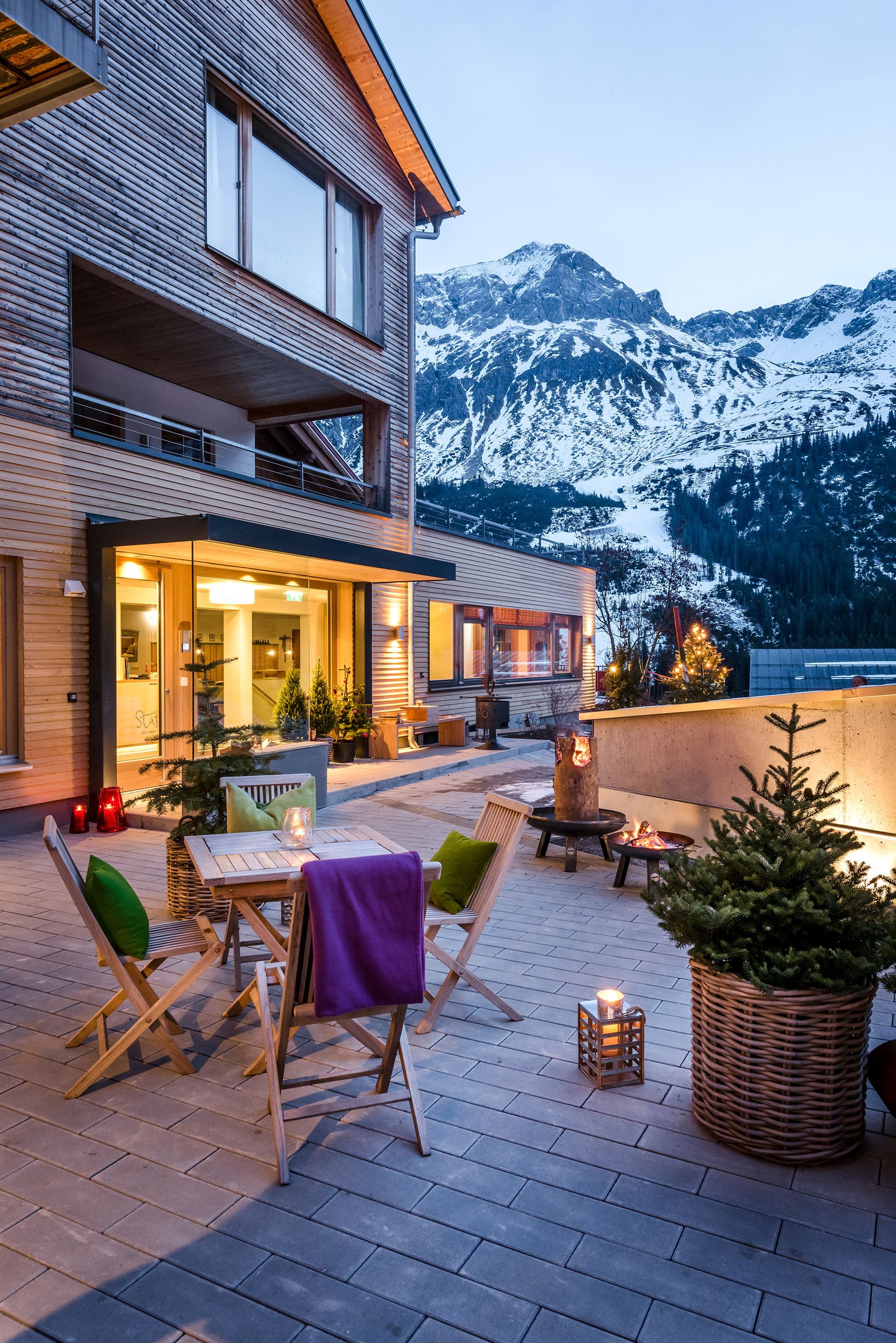 eine Terrasse mit einem Tisch und Stühlen vor einem Gebäude mit Bergen im Hintergrund .