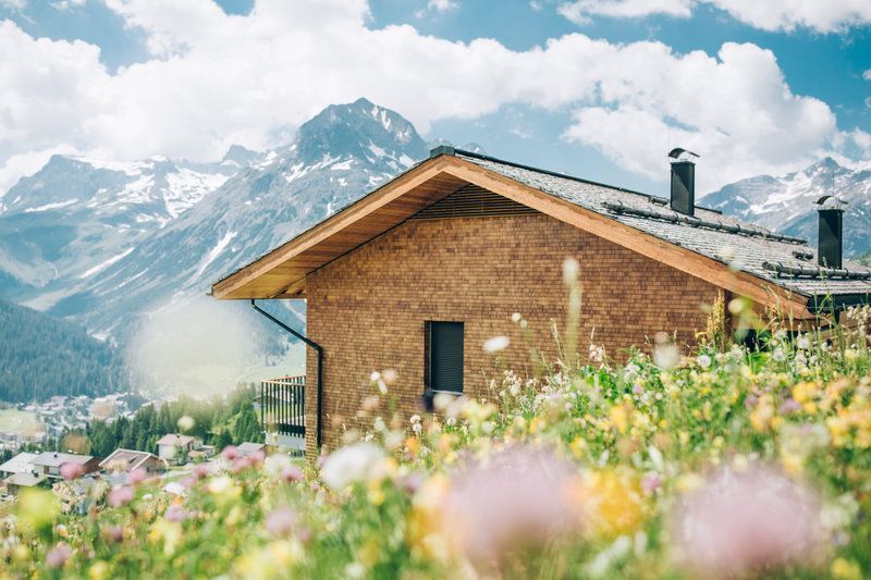 ein Haus steht inmitten eines Blumenfeldes mit Bergen im Hintergrund .