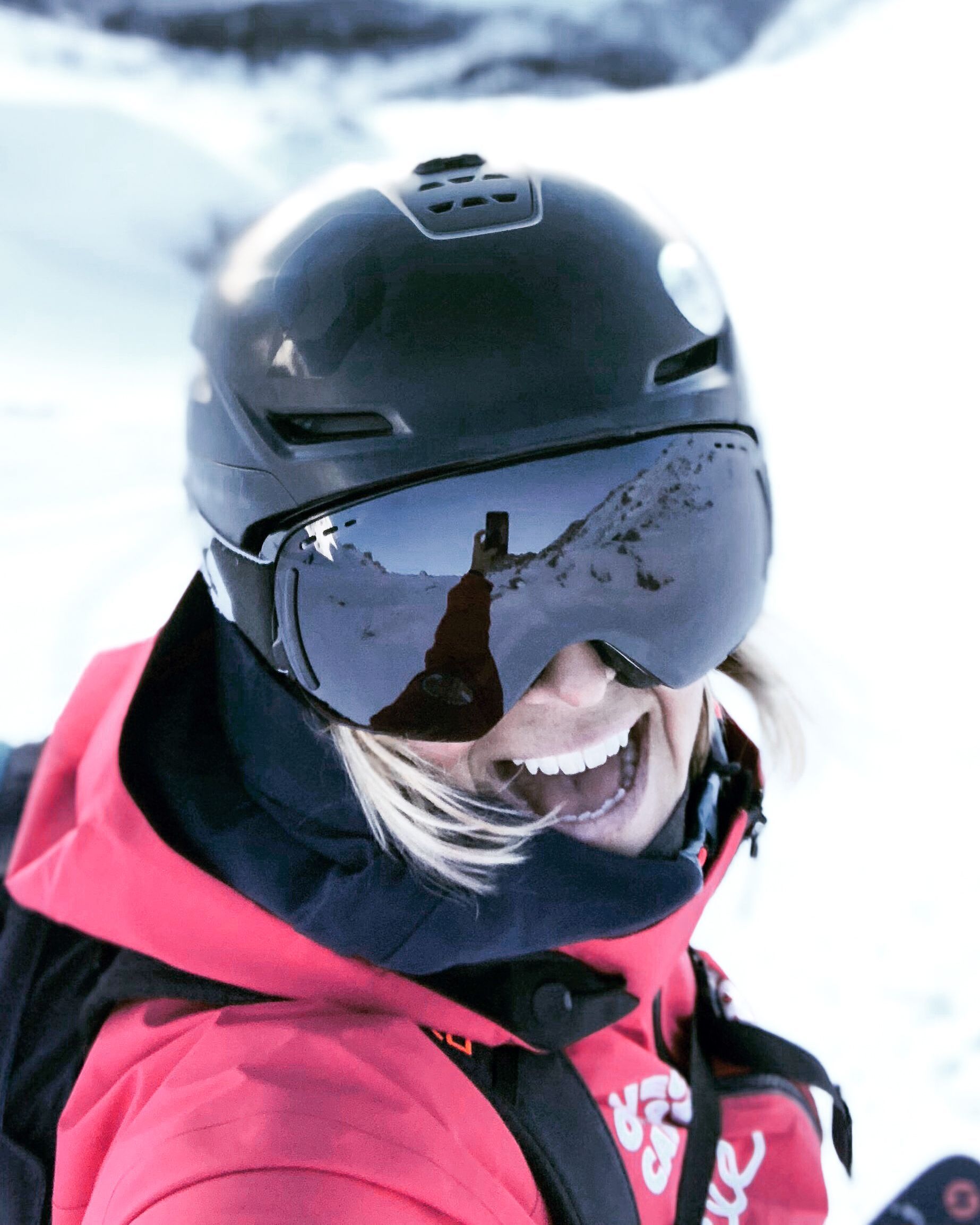 eine Frau trägt einen Helm und eine Skibrille und lächelt