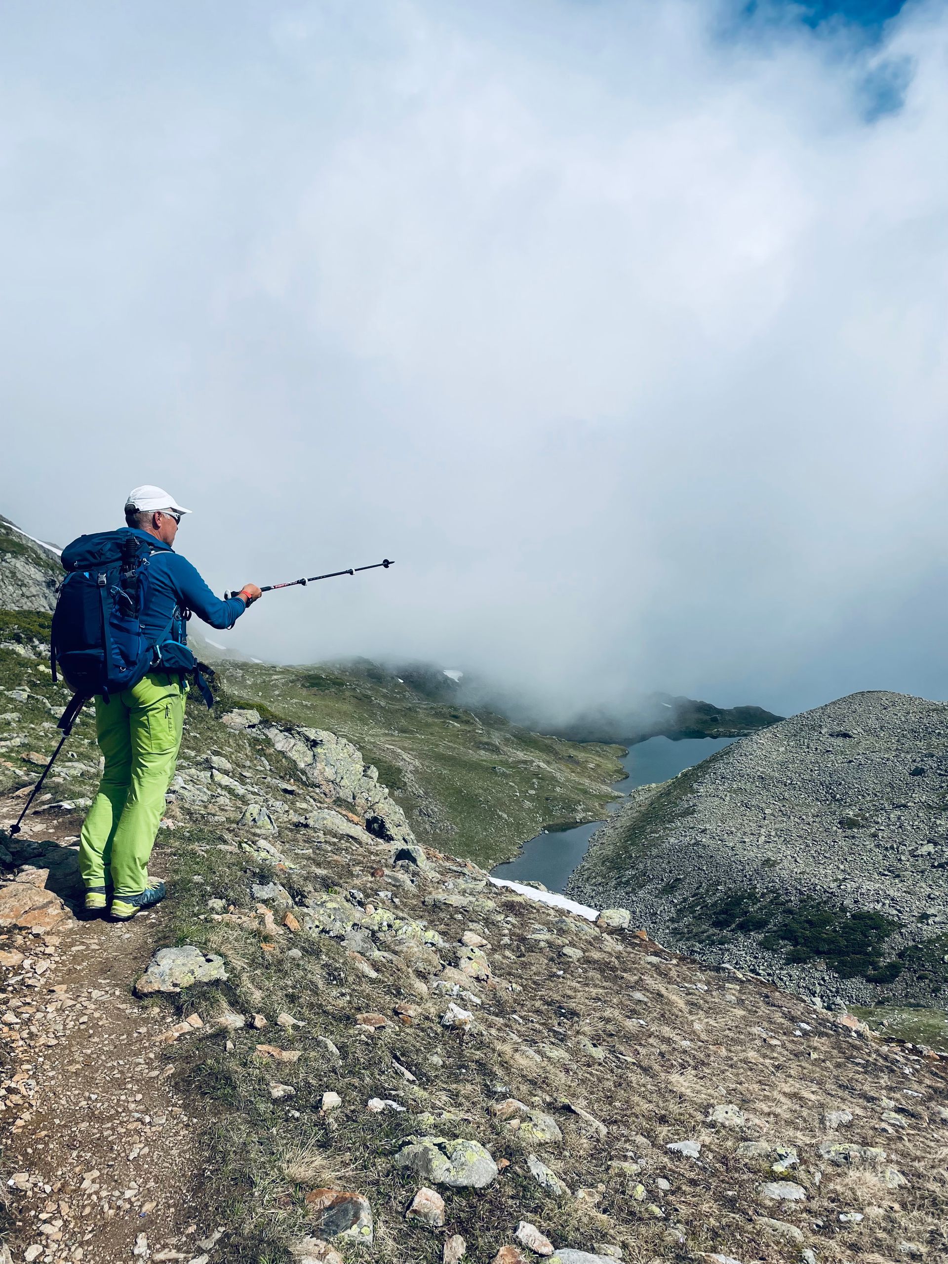 Ein Mann mit Rucksack und Wanderstöcken geht auf einem Bergpfad .
