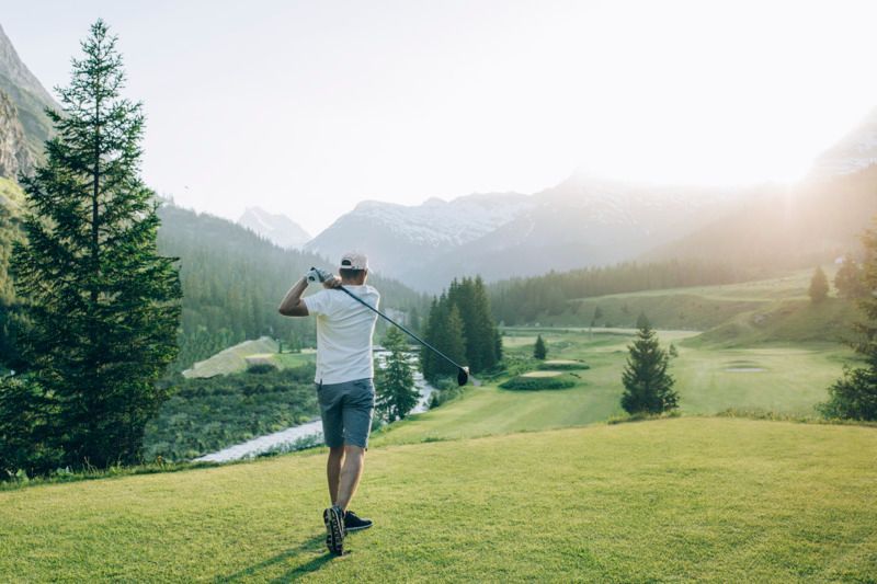 Ein Mann spielt Golf auf einem Golfplatz mit Bergen im Hintergrund .