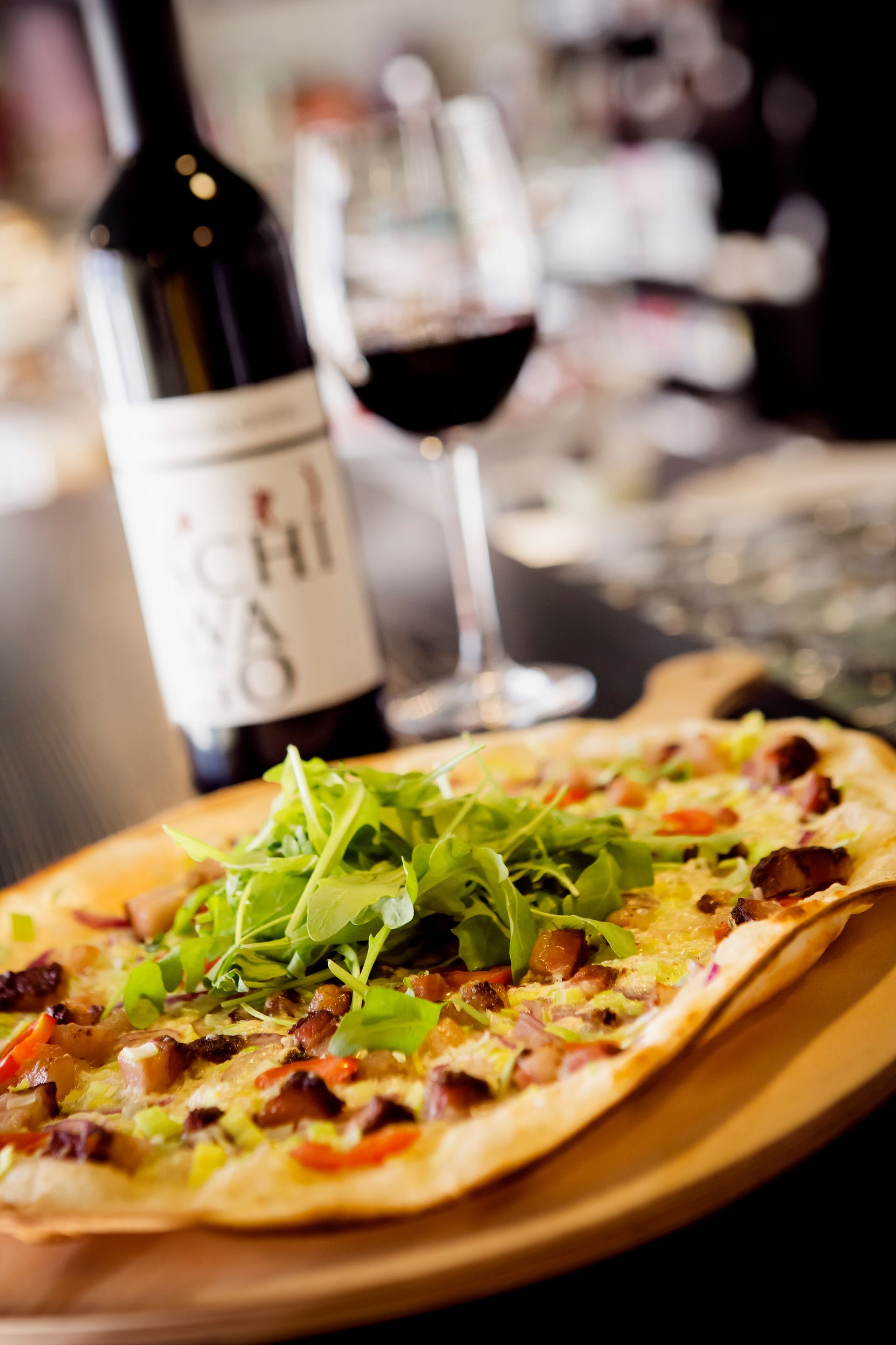 eine Pizza liegt auf einem Holzbrett neben einer Flasche Wein und einem Glas Wein .