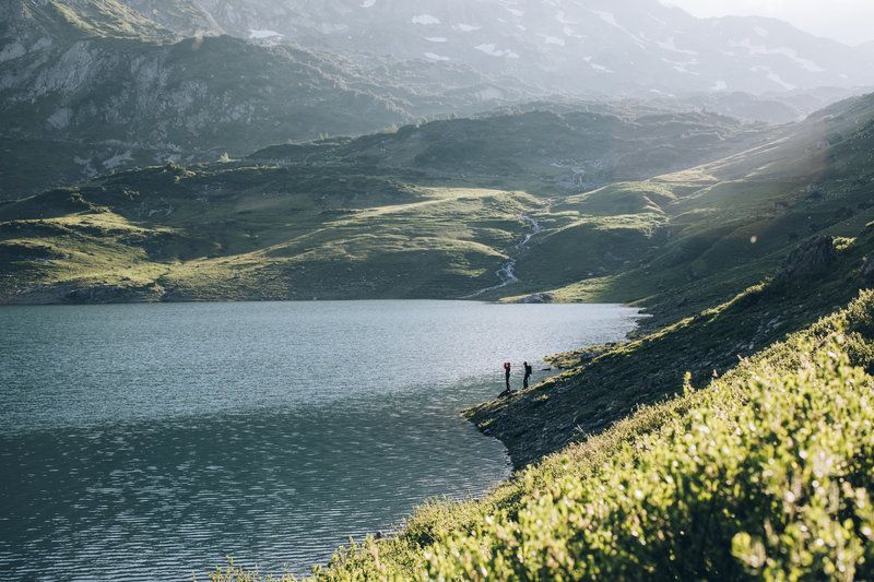 Menschen stehen am Rand eines Sees in den Bergen .