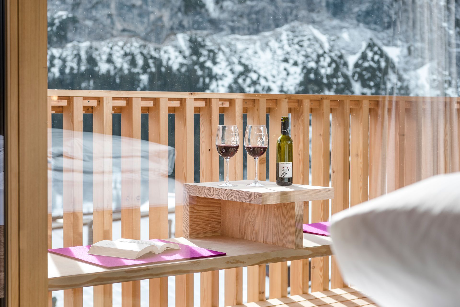 Auf einem Holzbalkon steht ein Tisch mit zwei Gläsern Wein und einer Flasche Wein .