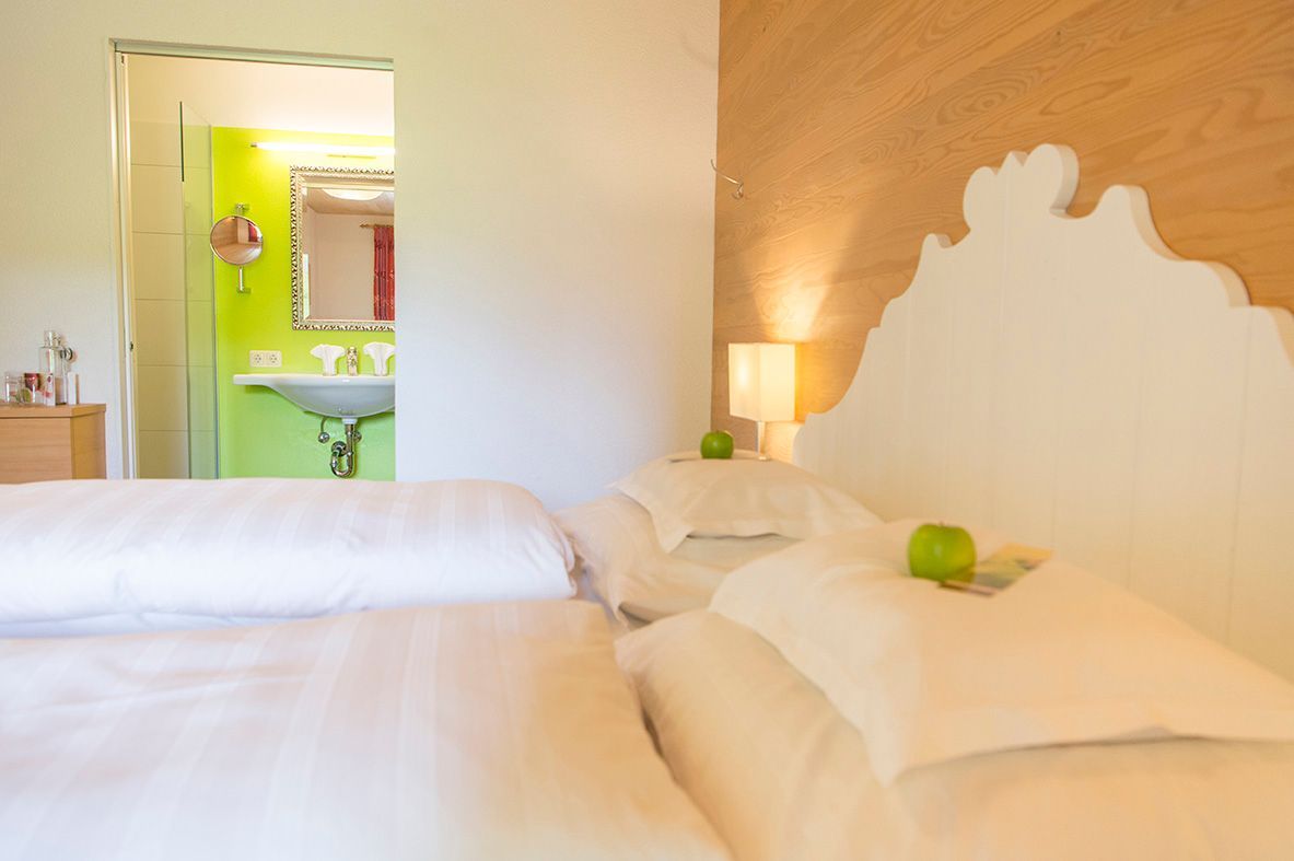 Hotelzimmer mit weissem Holzdoppelbett und einem Badezimmer im Hintergrund