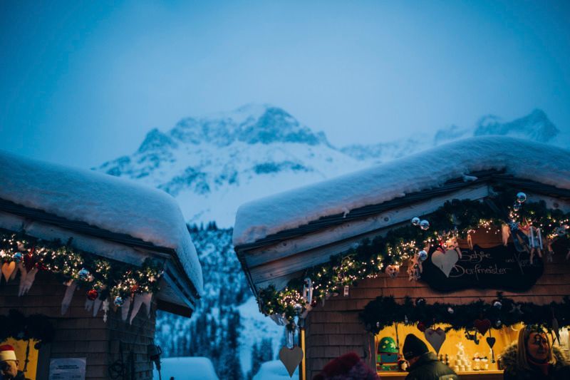 ein Weihnachtsmarkt mit schneebedeckten Häusern und Bergen im Hintergrund .