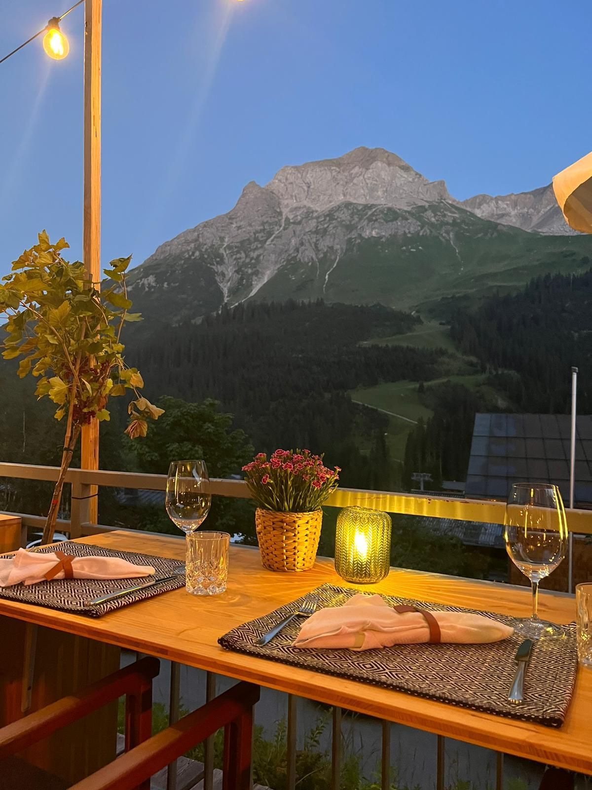 ein Tisch mit Weingläsern und Blumen auf einem Balkon mit Blick auf die Berge