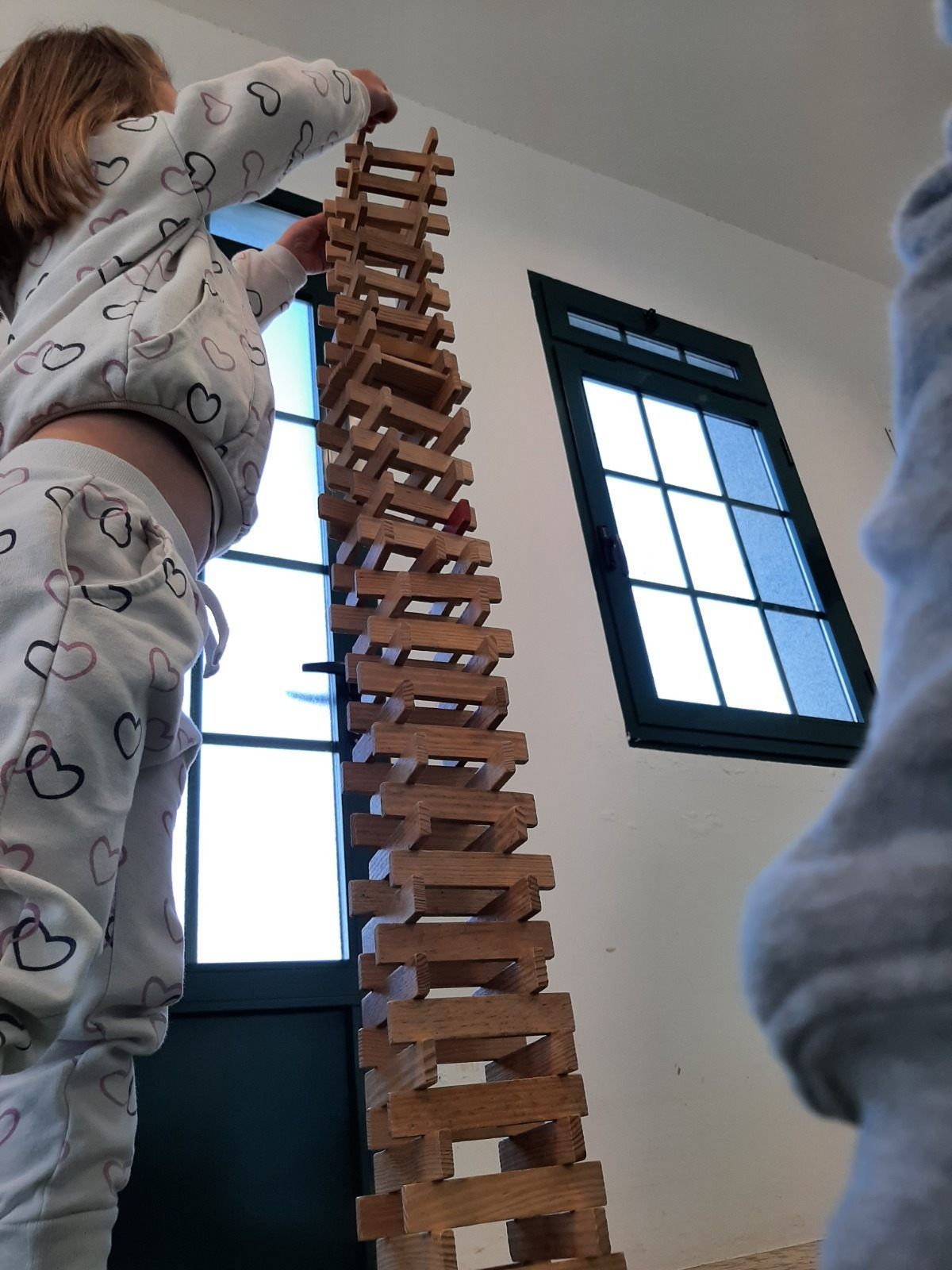 Niño construyendo una torre alta con bloques de madera cerca de una ventana.