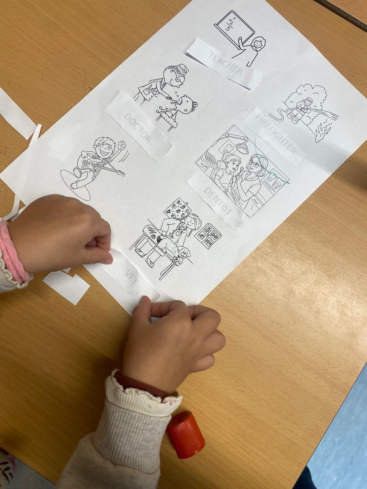 Dos personas en el escenario sosteniendo papeles, hablando. Auditorio iluminado con luz naranja, público visible.