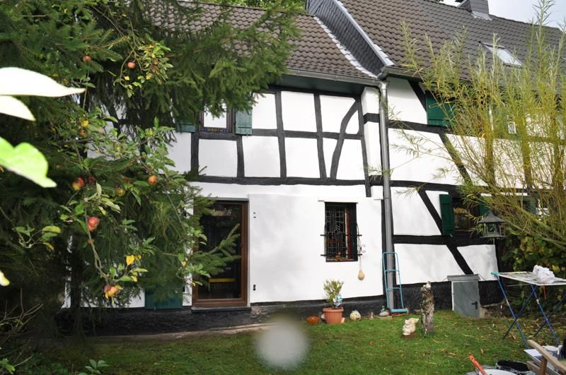 Ein weißes Haus mit schwarzen Verzierungen ist von Bäumen umgeben