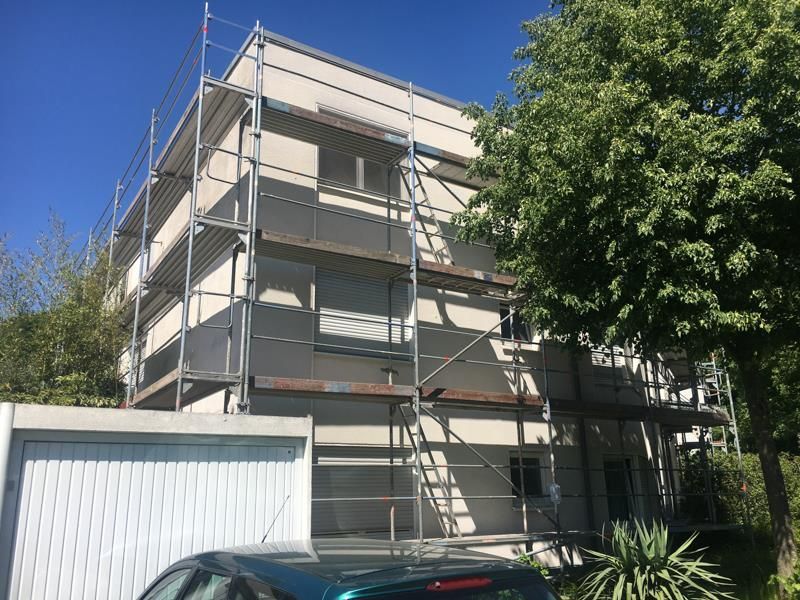 Vor einem Gebäude mit einem Gerüst ist ein Auto geparkt.