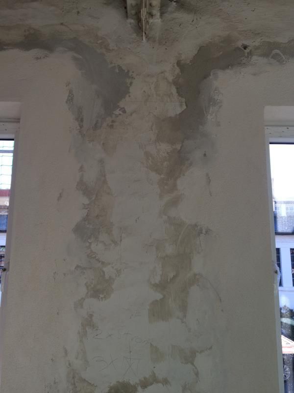 Eine weiße Wand mit abblätternder Farbe und ein Fenster in einem Zimmer.