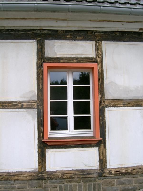 Ein weißes Fenster mit einem orangefarbenen Rahmen an einer Ziegelwand