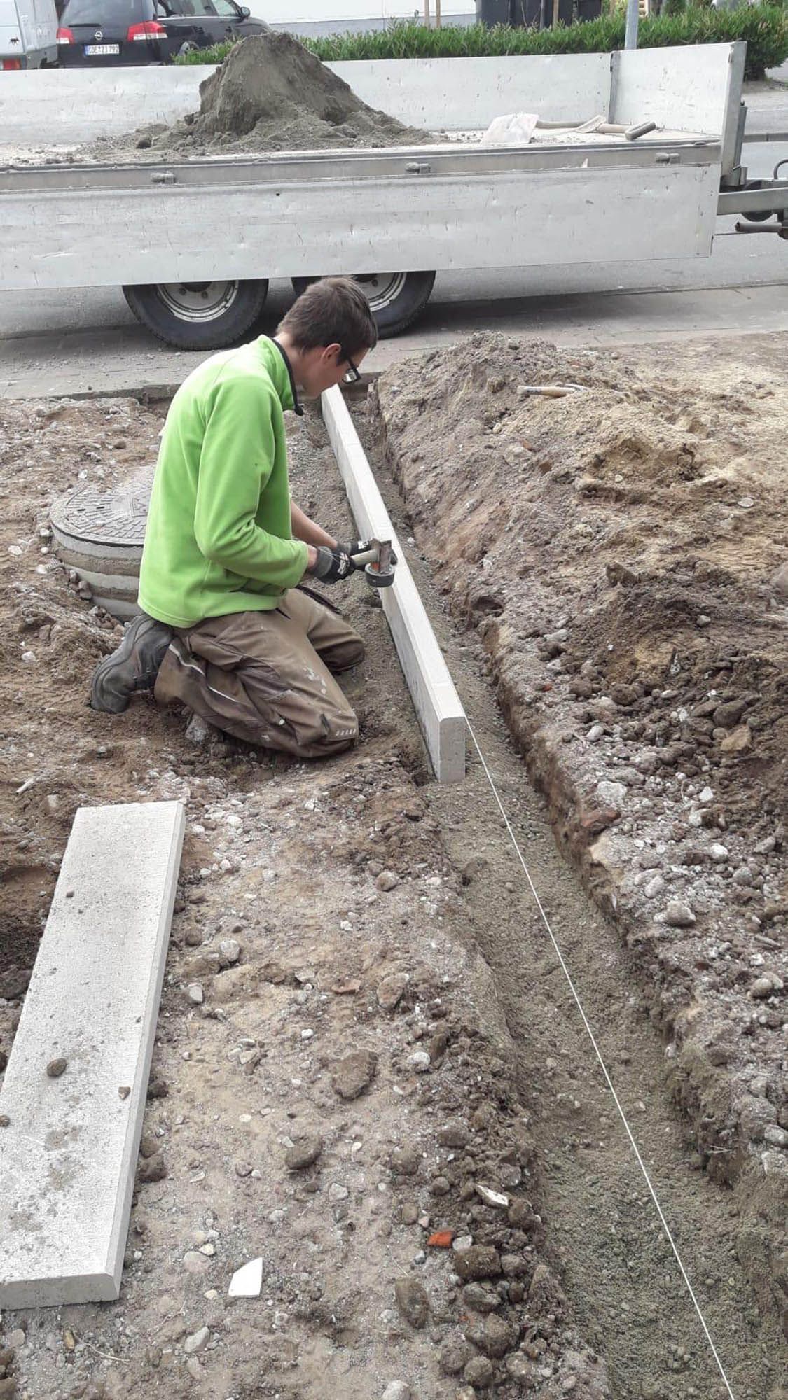 Ein Mann in einer grünen Jacke kniet im Dreck.