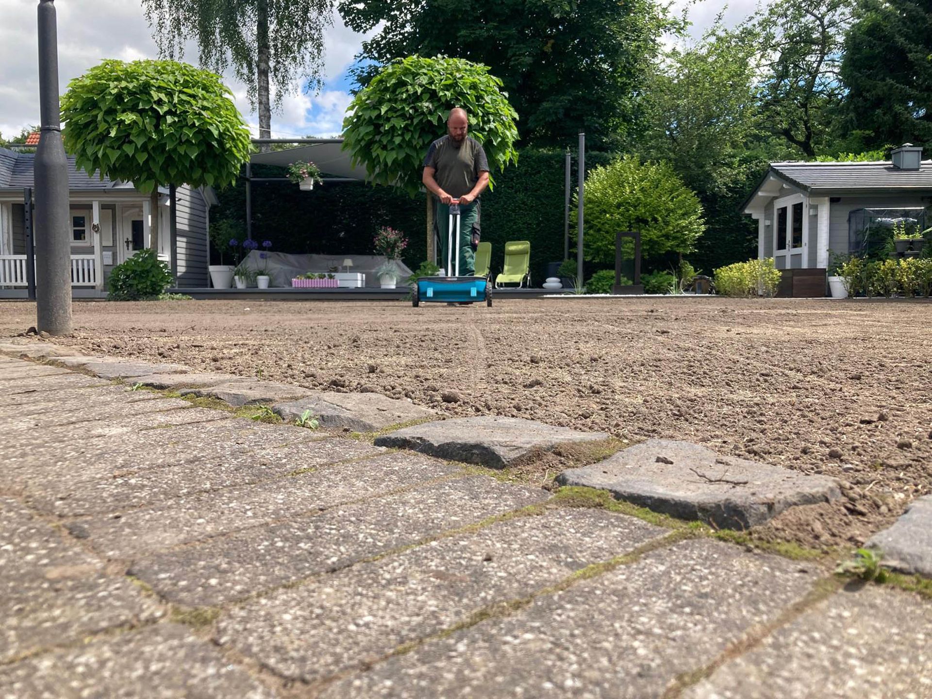 Ein Mann steht mit einem Rasenmäher in einem Hof.