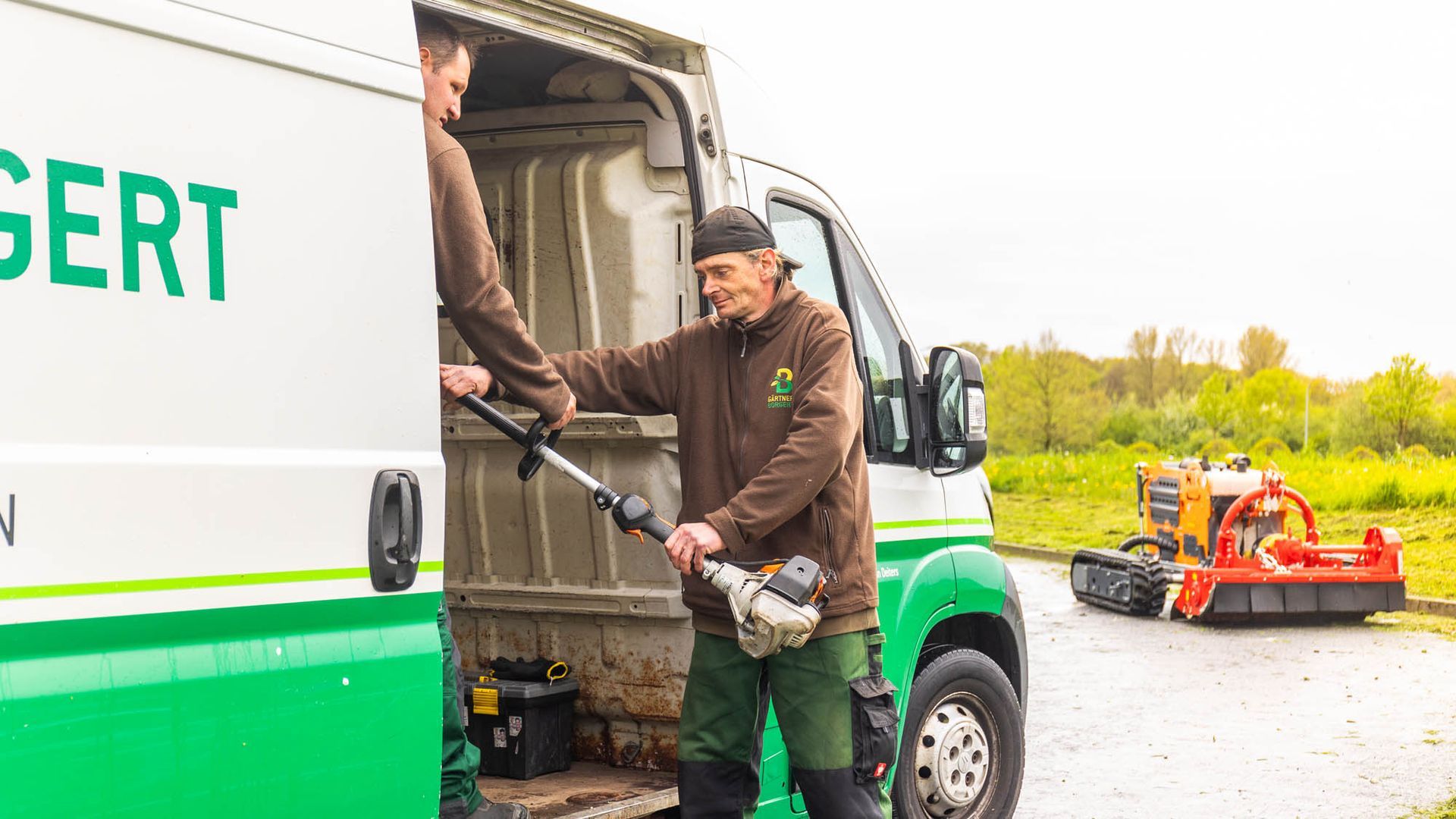 Ein Mann holt einen Rasenmäher aus einem Lieferwagen.
