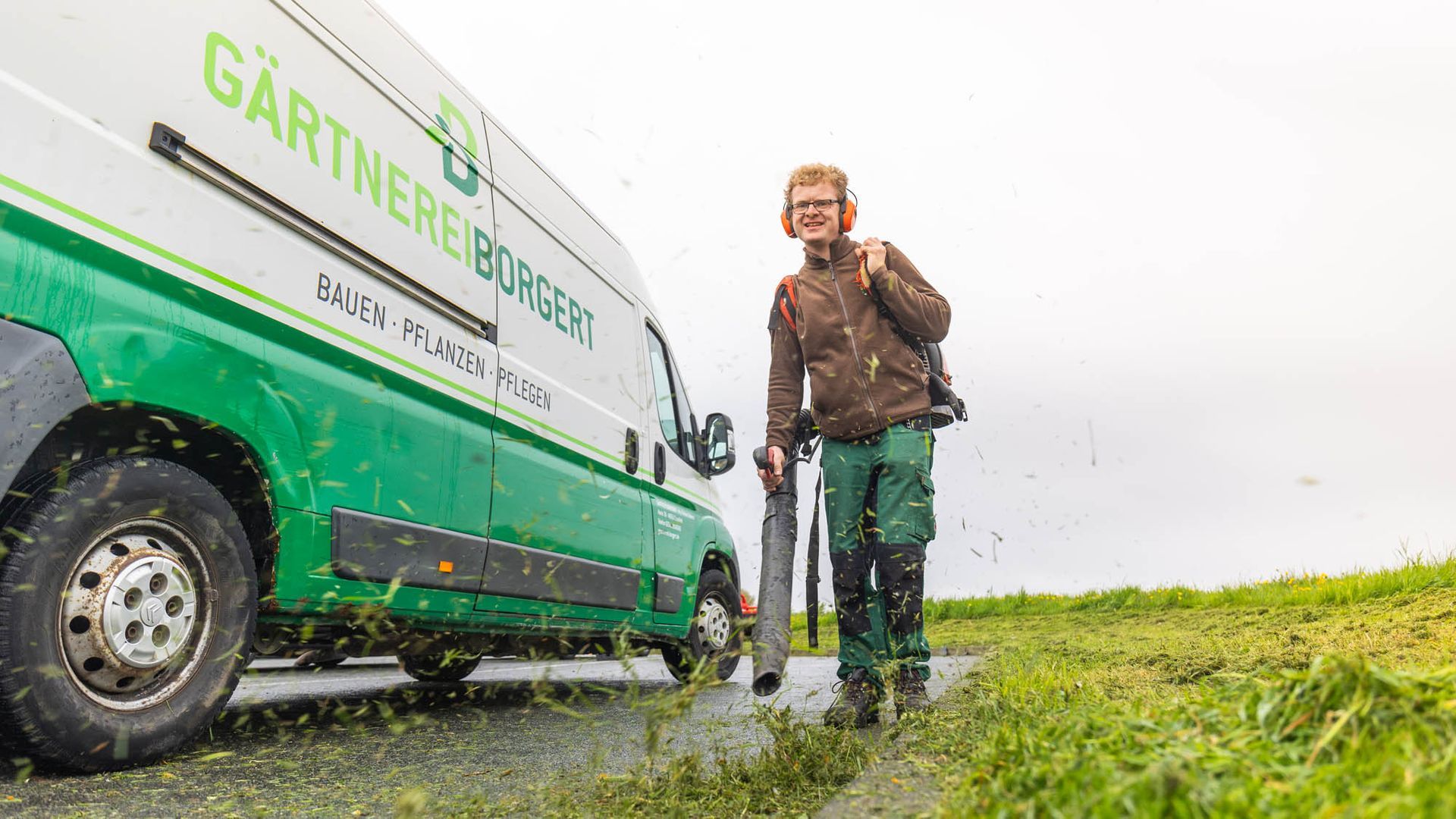 Ein Mann mäht das Gras vor einem grünen Lieferwagen.