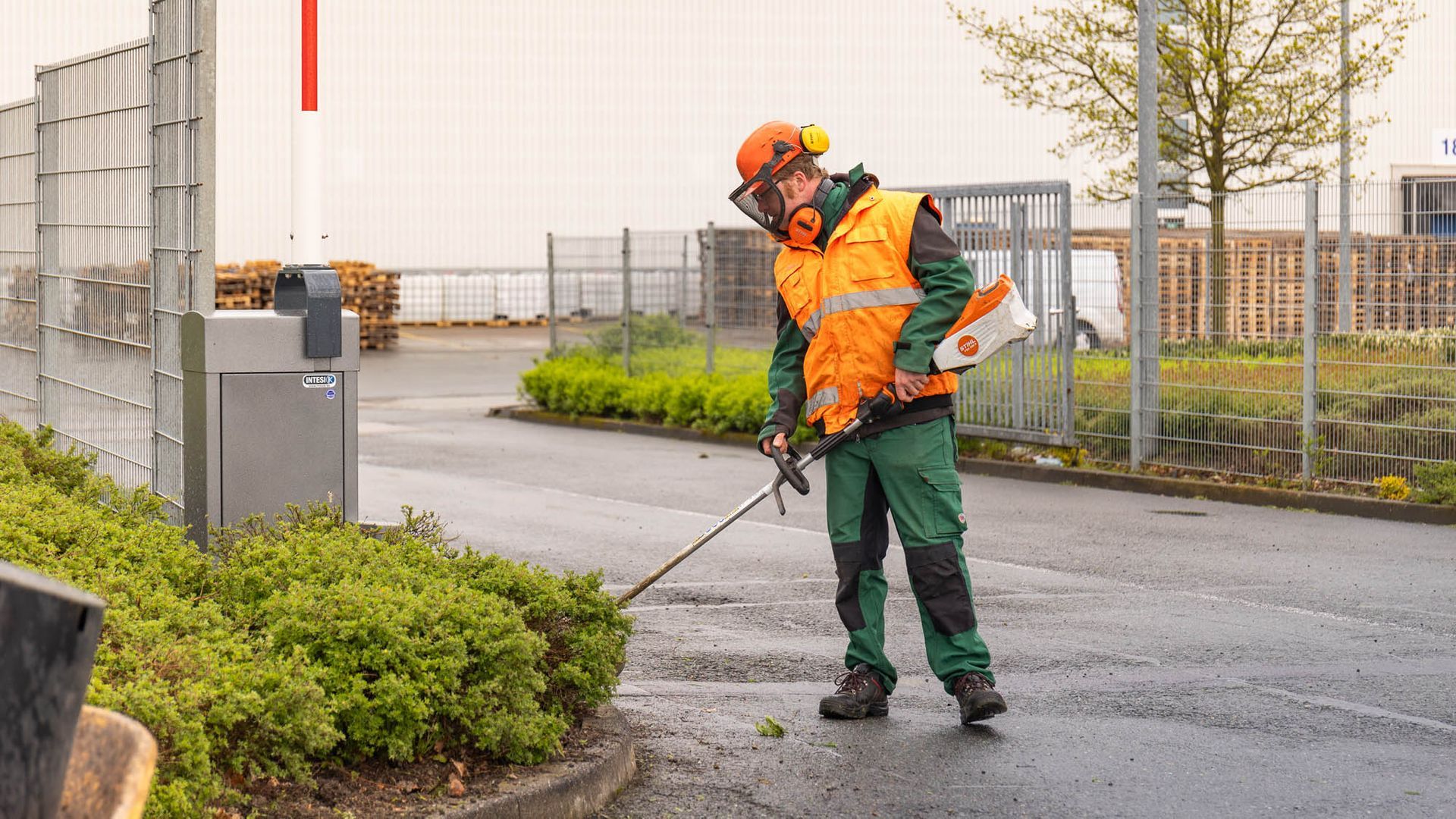 Ein Mann schneidet mit einem Rasenmäher Pflanzen am Straßenrand.