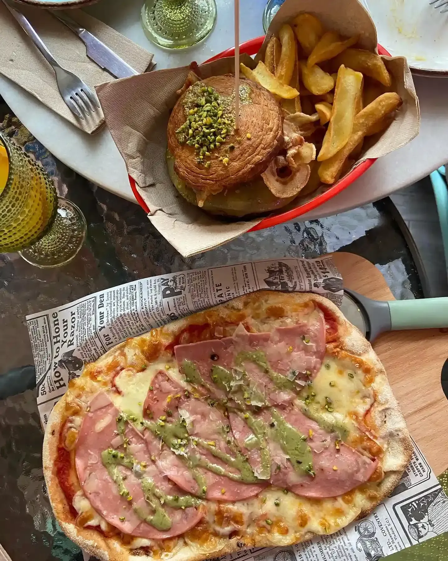 Vista aérea de una comida con hamburguesa, papas fritas y pizza en bandejas forradas con papel de periódico en una mesa.
